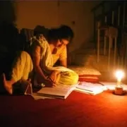 A woman reading a book with a candle as her only source of light