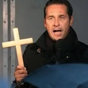 A man holding a wooden cross and speaking into a microphone