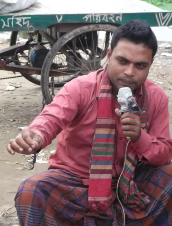 A man sitting on the ground holding a microphone in one hand an a scorpion in the other hand.