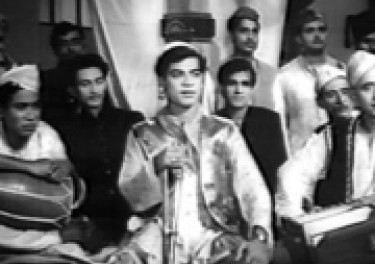 Scene from an old Hindi film of a group of people sitting cross-legged on the floor