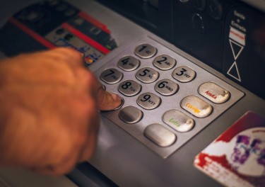 person holding white and red card using a ATM - Hand pressing number